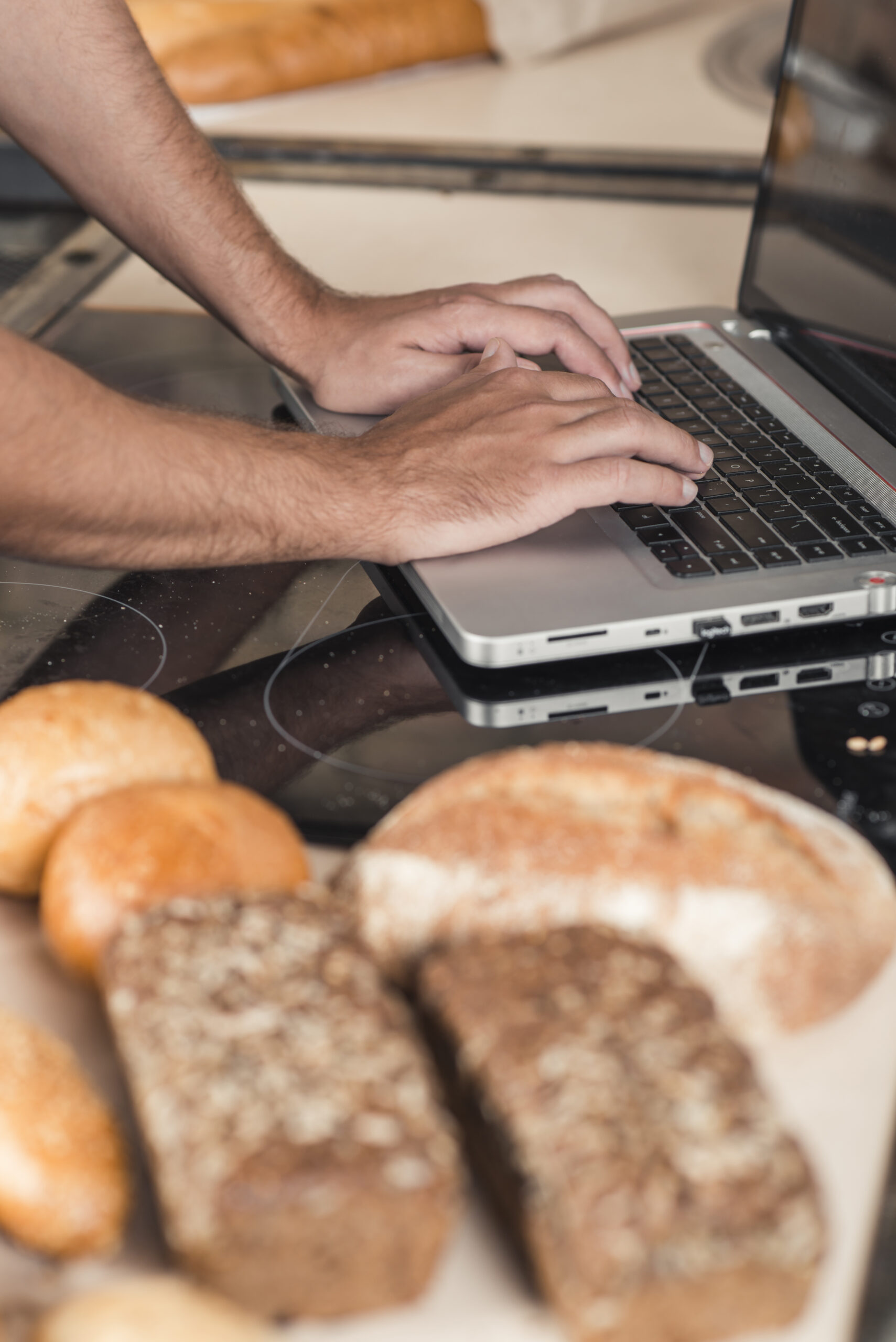 main-de-baker-tapant-sur-un-ordinateur-portable-sur-le-plan-de-travail-de-la-cuisine-avec-des-pains-cuits